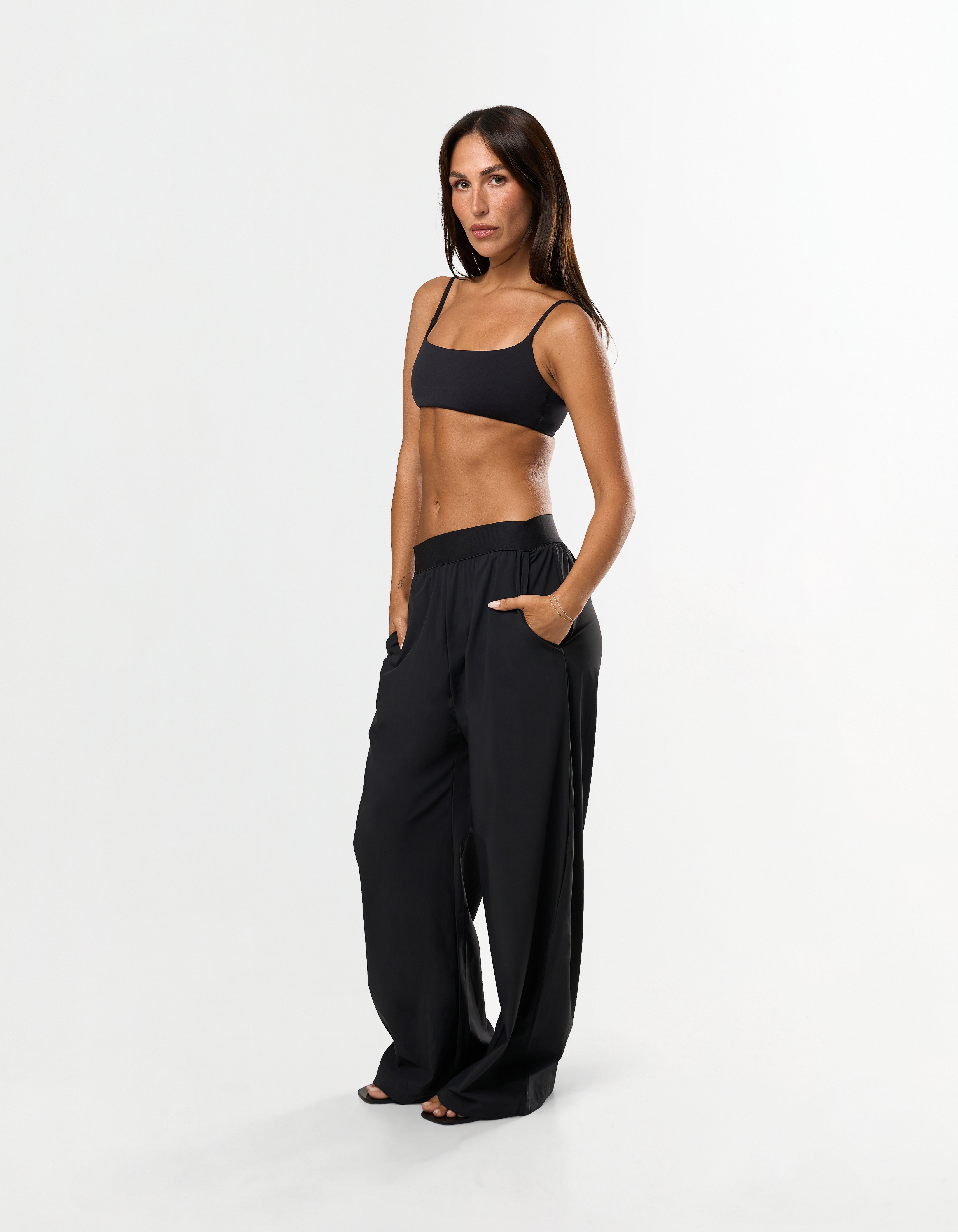 Front view of model wearing STAX. Gigi Pants in black showing outer elastic waistband design paired with black sports bra