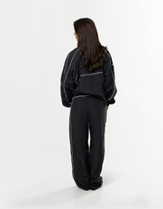 Back view of model wearing STAX. Woven Track Jacket in black with matching Track Pants