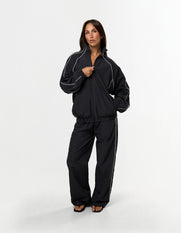 Front view of model wearing STAX. Woven Track Jacket zipped up with matching track pants