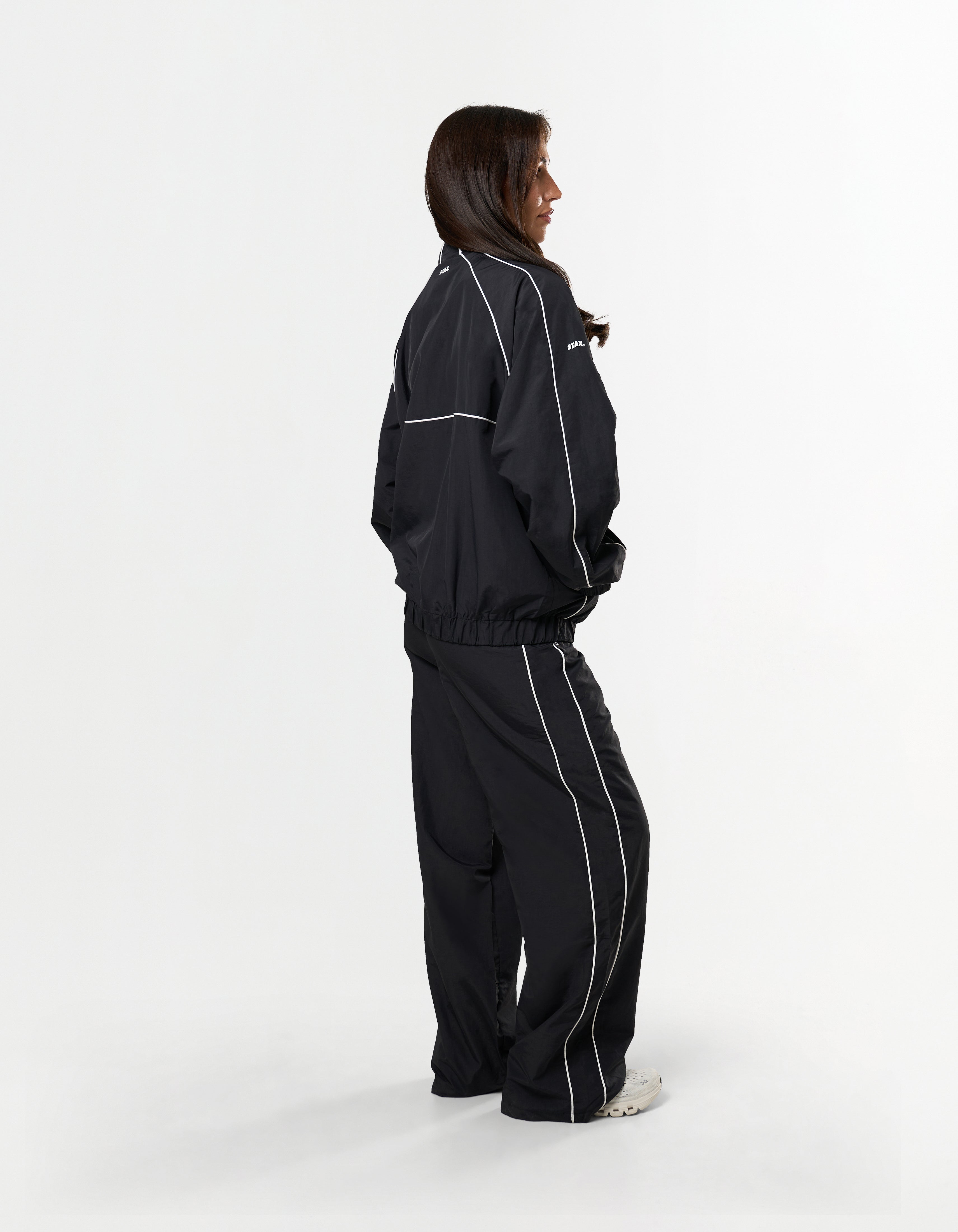 Side over the shoulder view of model wearing STAX. Woven Track Jacket 