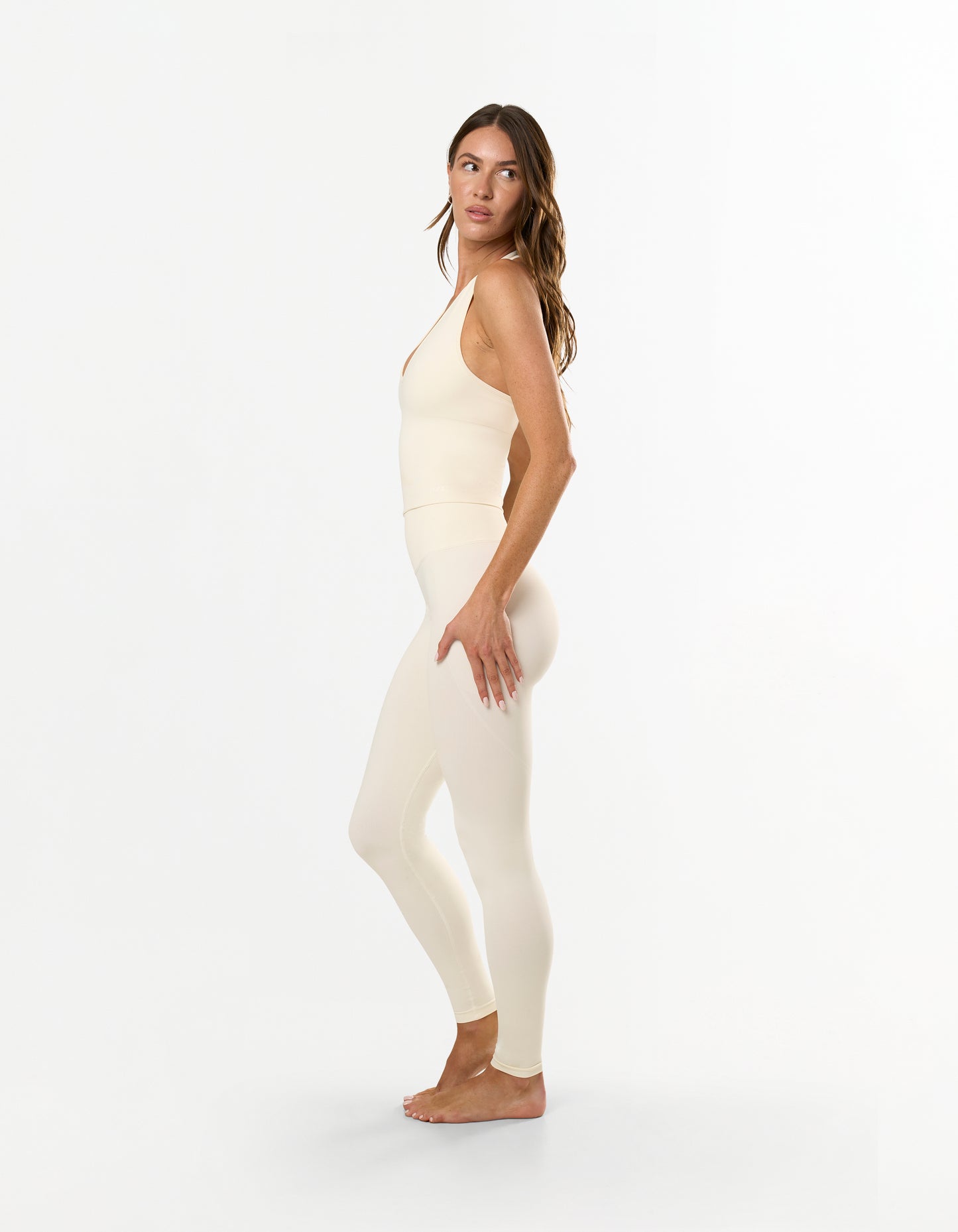 Side profile of model wearing STAX. Premium Seamless Skulpt Leggings in Cream with compressive ribbed waistband and invisible contouring scrunch