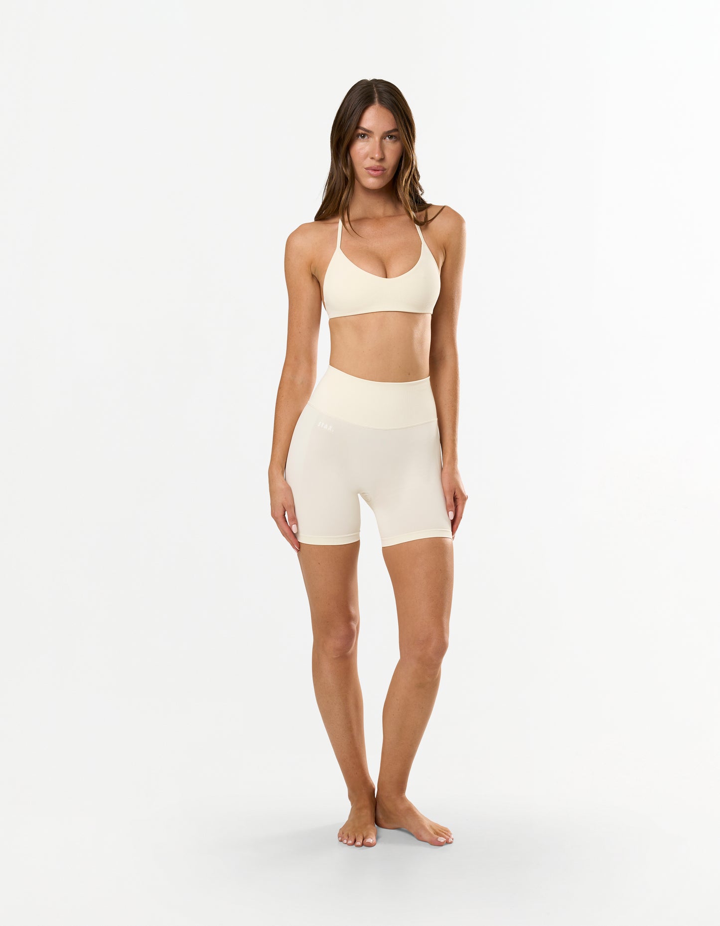 Front view of model wearing STAX. Premium Seamless Skulpt Bralette in Cream with matching skulpt midi bike shorts 