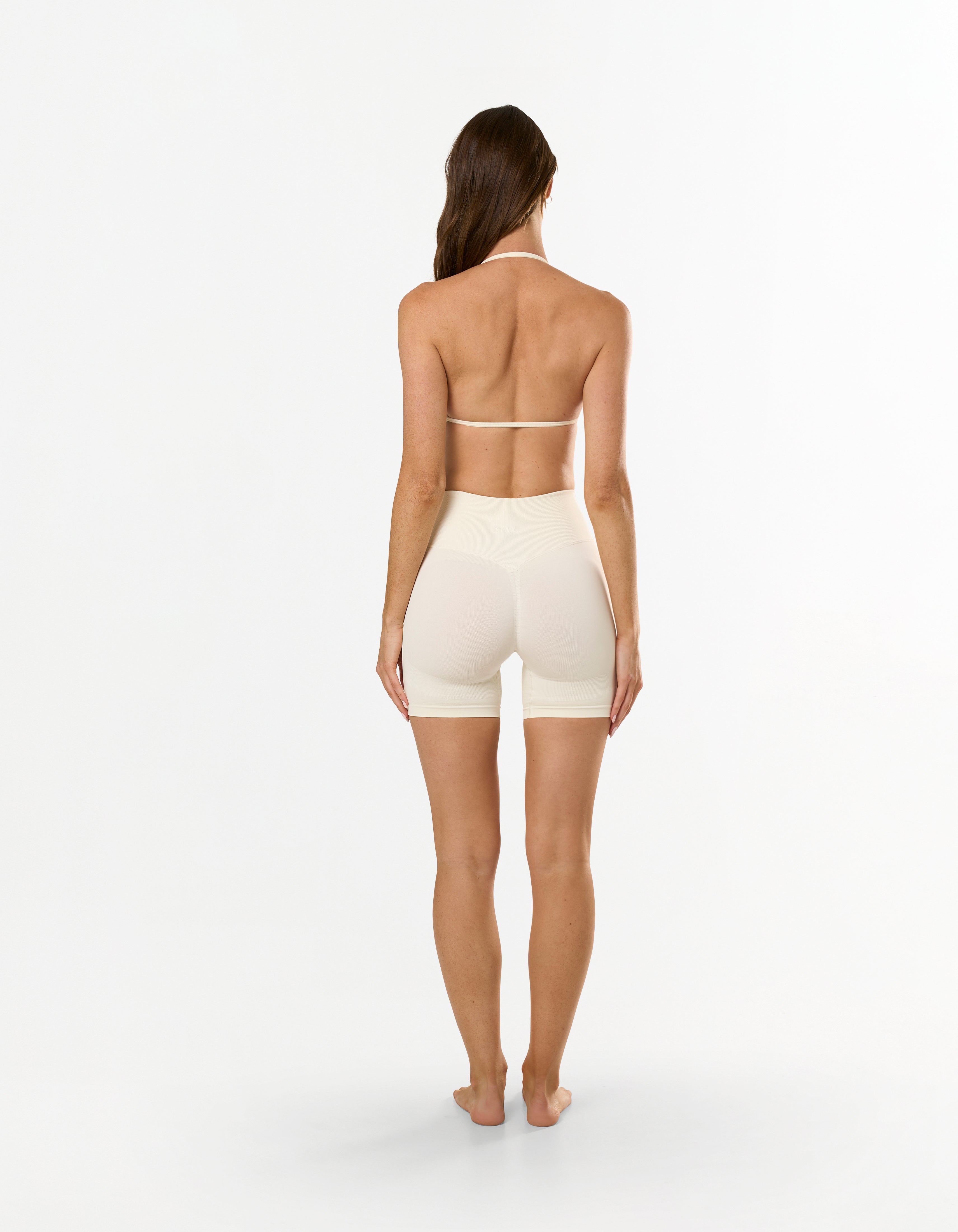 Back view of model wearing STAX. Premium Seamless Skulpt Midi Bike Shorts in Cream showing curve enhancing compressive fit