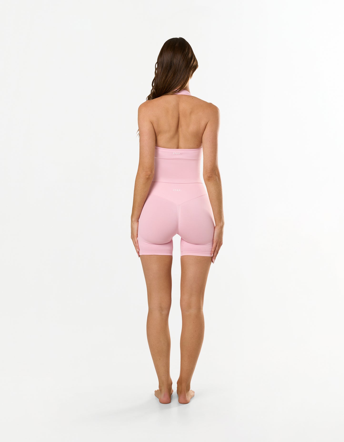 Back view of model wearing STAX. Premium Seamless Skulpt Midi Bike Shorts in Pink showing flattering V back glute contouring seam