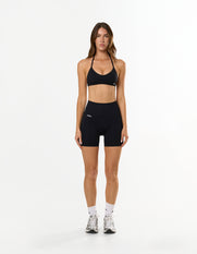 Front view of model wearing STAX. Premium Seamless Skulpt Midi Bike Shorts  in Black showing premium nylon spandex fabric with printed silicone logo 