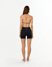Back view of model wearing STAX. Premium Seamless Skulpt Midi Bike Shorts   in Black showing flattering invisible scrunch detail and matching strappy halter neck bralette