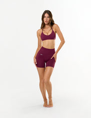Front view of model wearing STAX. Premium Seamless Skulpt Midi Bike Shorts in Burgundy with matching Burgundy Skulpt Bralette 