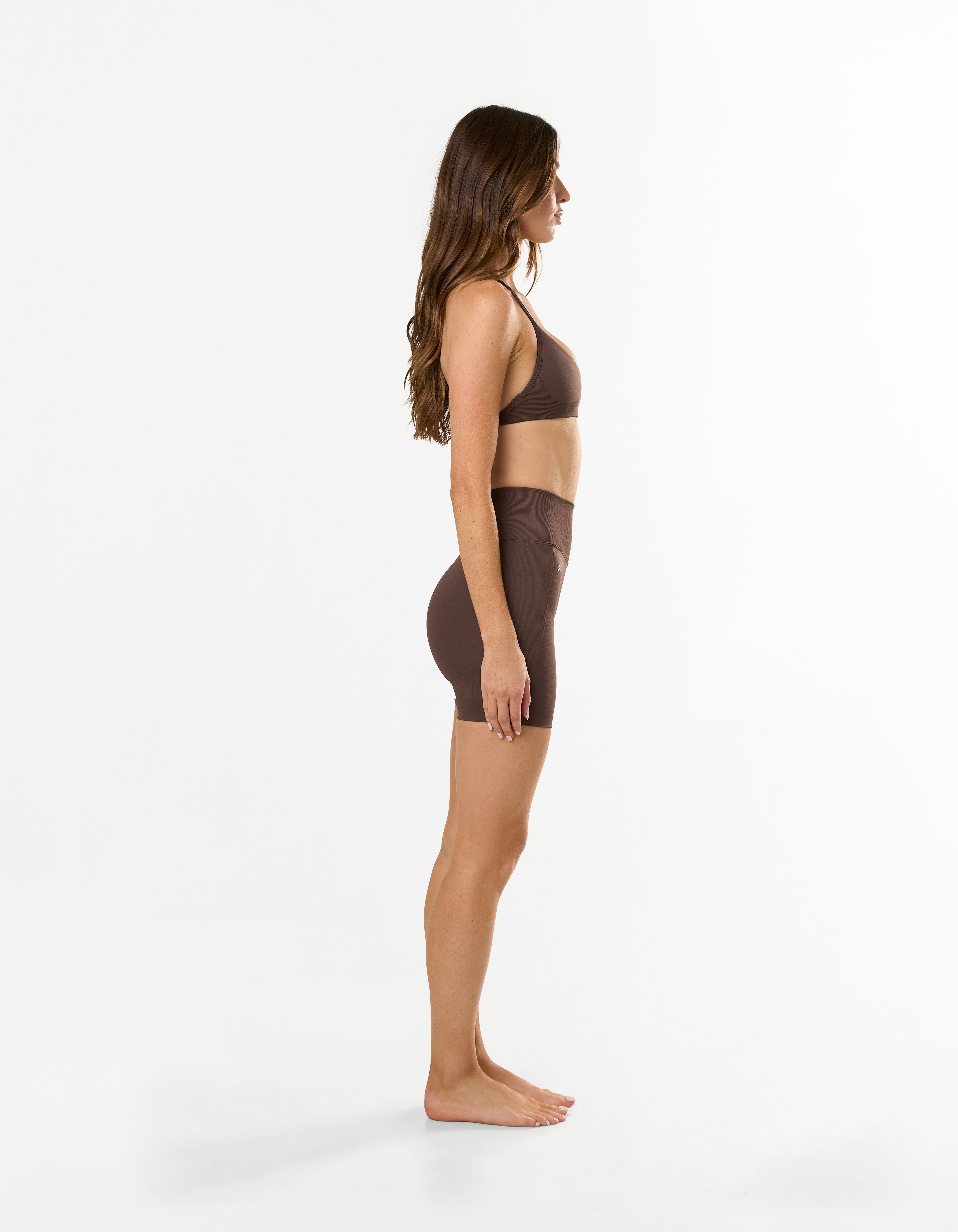Side view of model wearing STAX. Premium Seamless Skulpt Midi Bike Shorts in Brown showing compressive ribbed waistband 