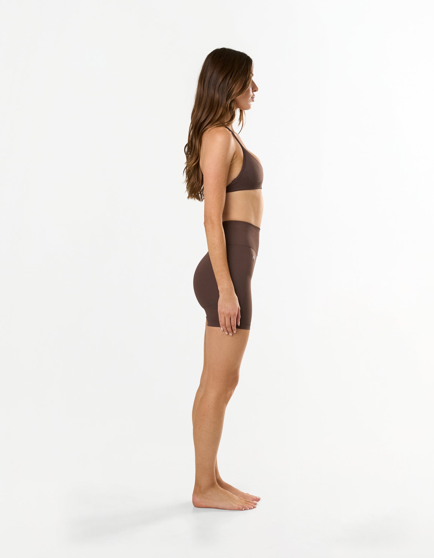 Side view of model wearing STAX. Premium Seamless Skulpt Midi Bike Shorts in Brown showing compressive ribbed waistband 