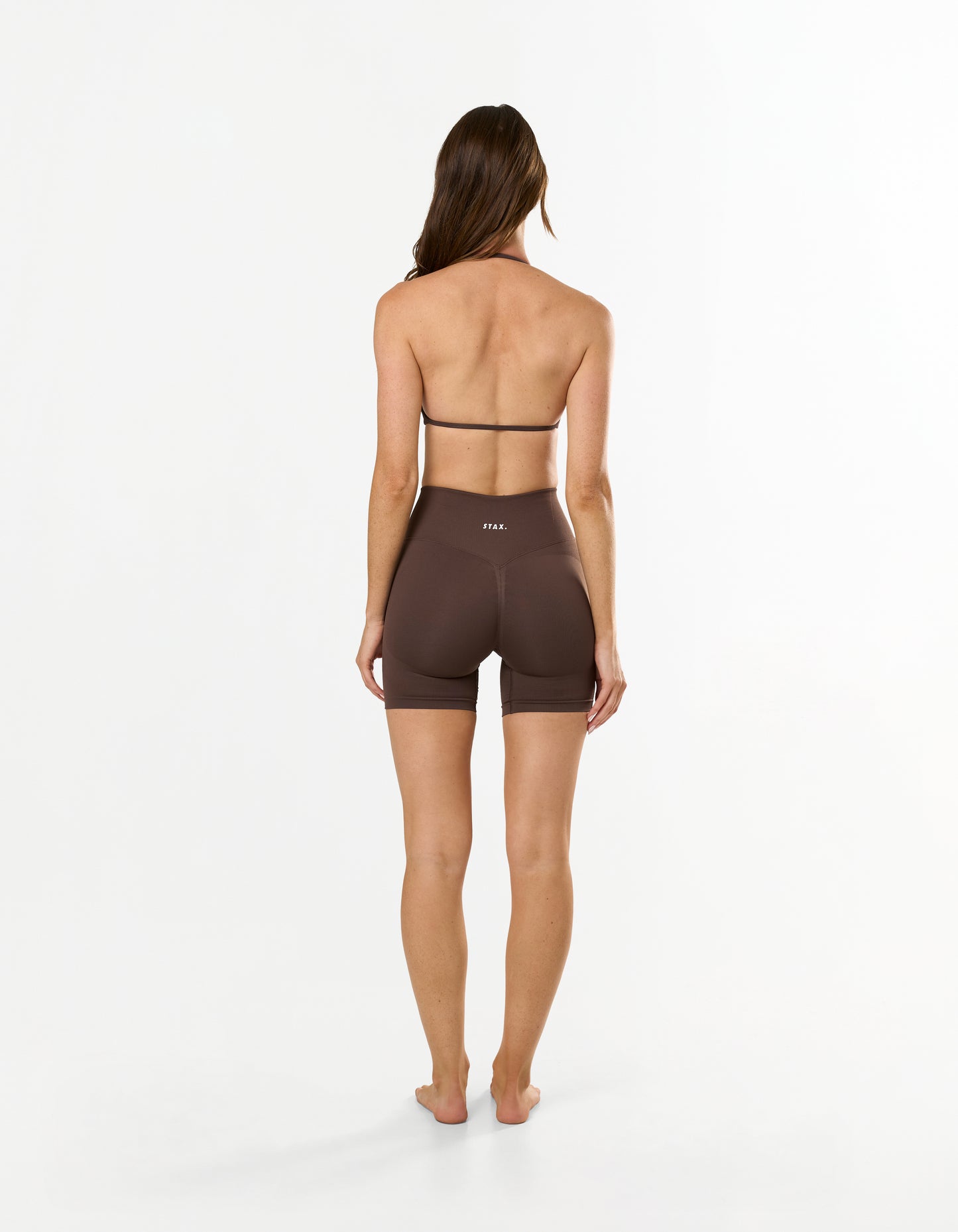 Back view of model wearing STAX. Premium Seamless Skulpt Midi Bike Shorts in Brown showing V back glute contouring seam
