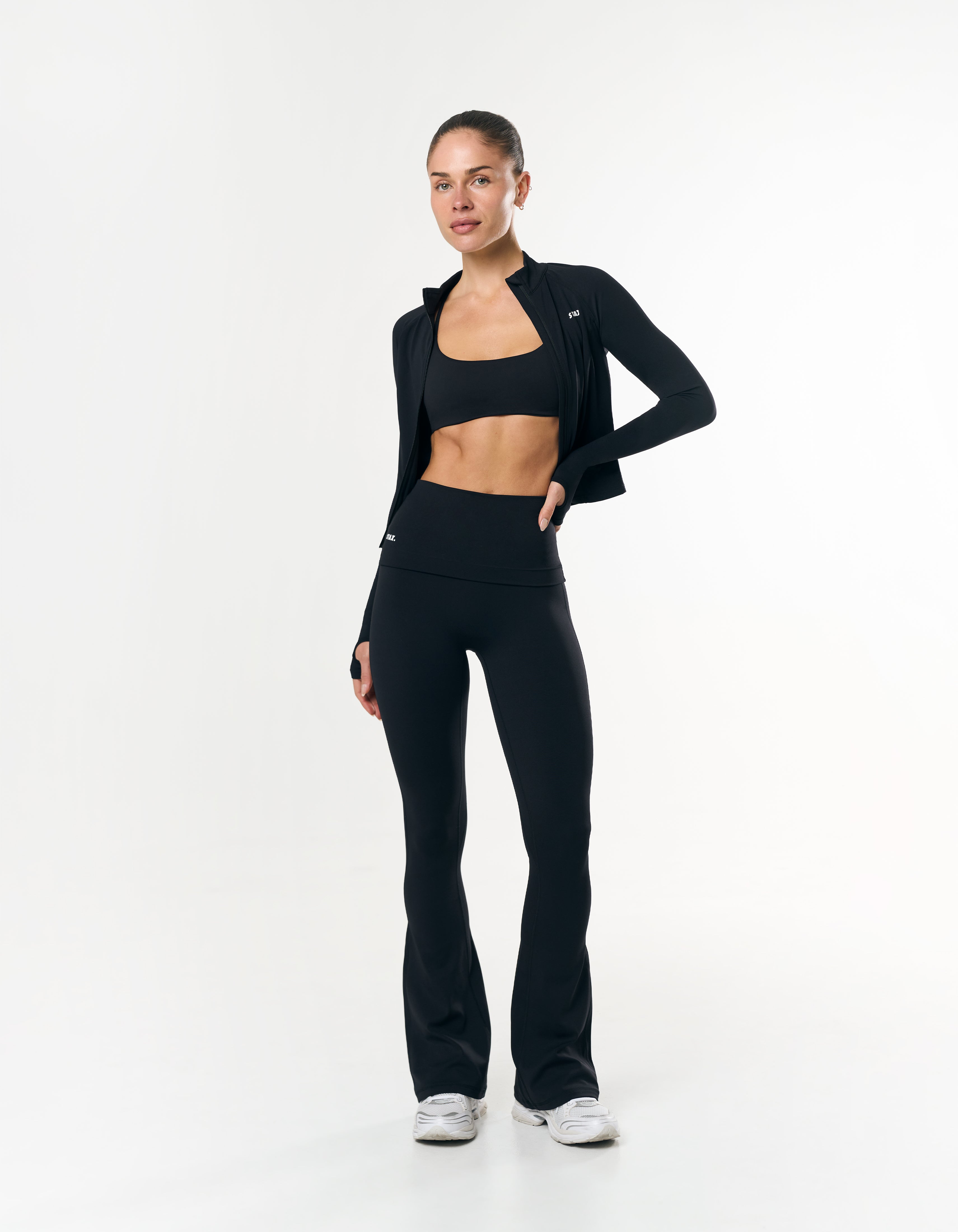 Front view of model wearing STAX. Fold Over Flares in Black with matching sports bra and active zip jacket in airlyte fabric 