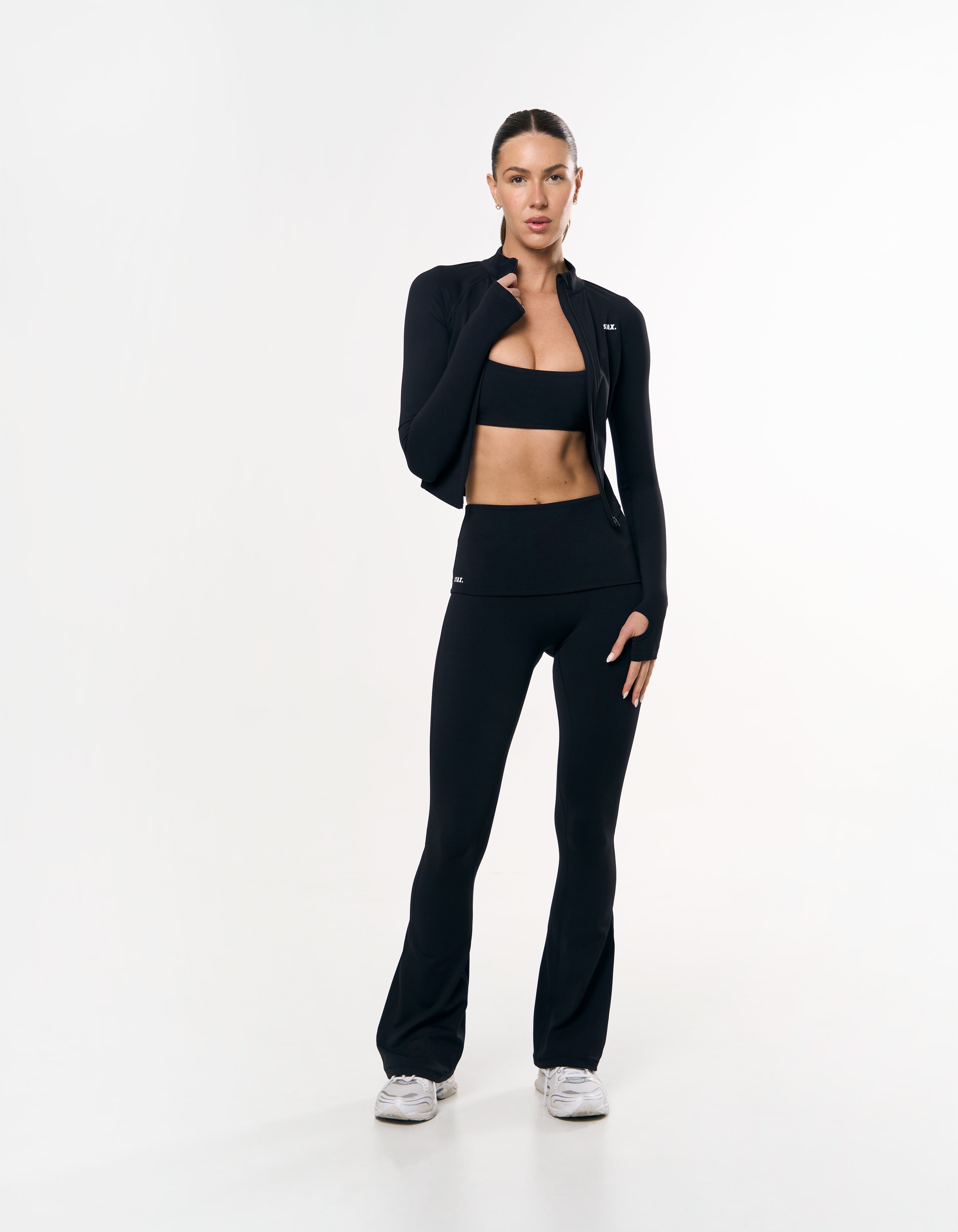 Front view of model wearing STAX. Active Zip Jacket Airlyte in Black with matching bandeau bra and flare tights