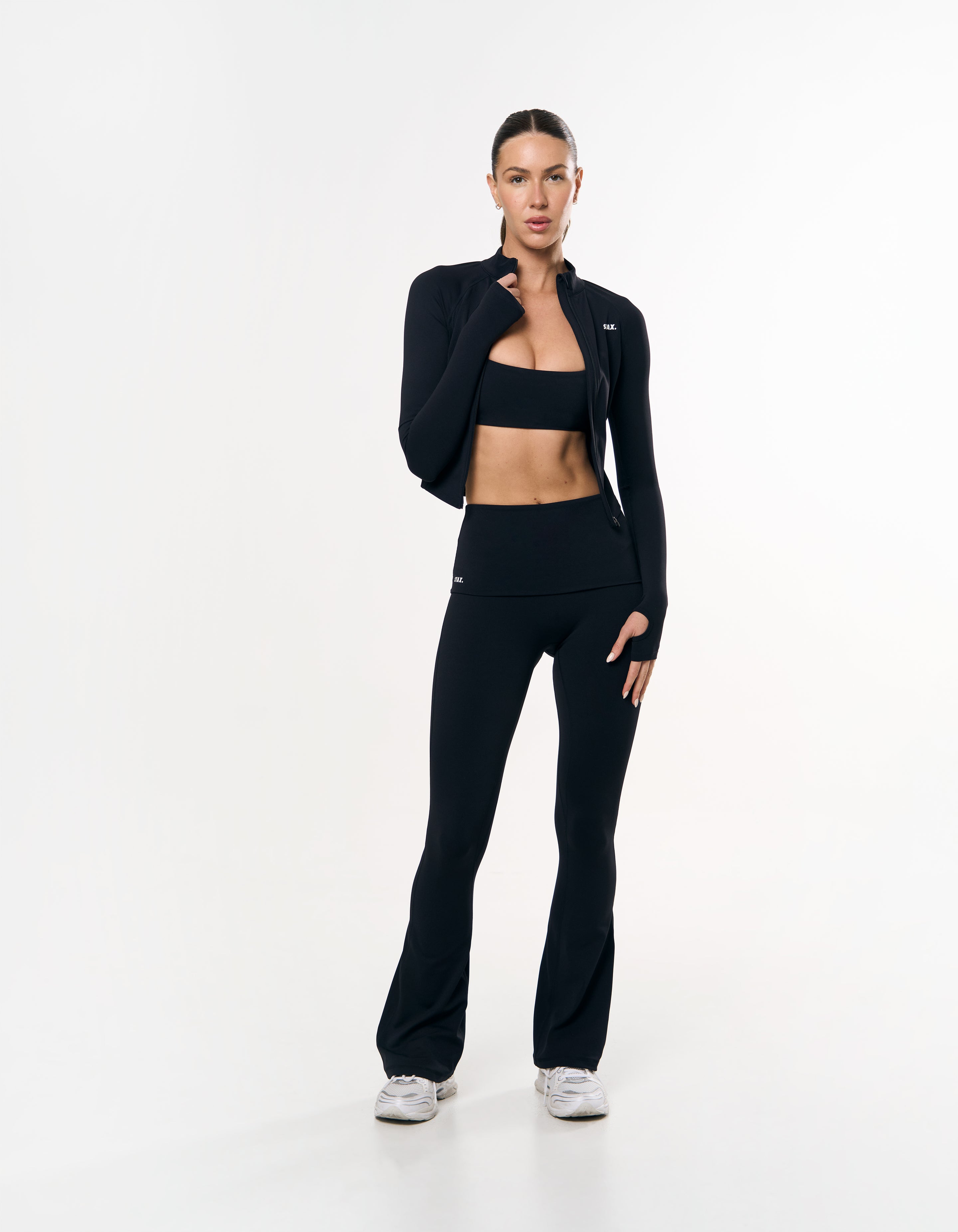 Front view of model wearing STAX. Active Zip Jacket Airlyte in Black with matching bandeau bra and flare tights